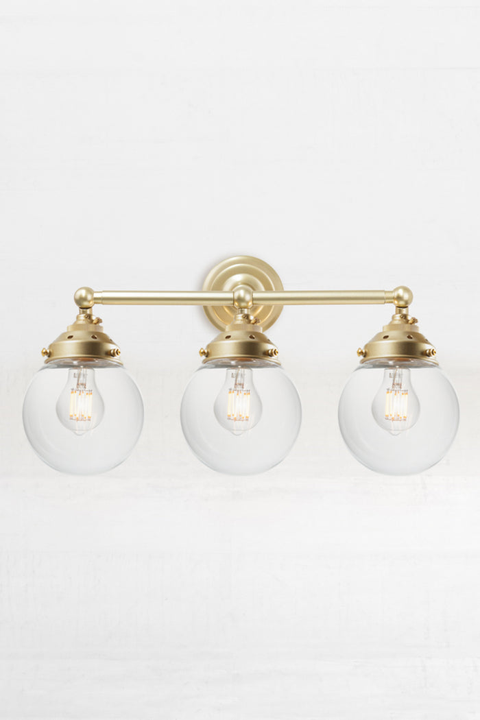 Front view of the triple lamp swivel arm wall sconce in gold/brass, with clear glass ball shades.