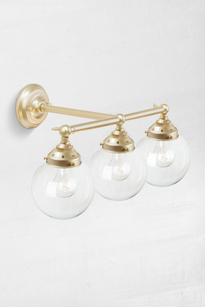 High view of the triple lamp swivel arm wall sconce in gold/brass, with clear glass ball shades.