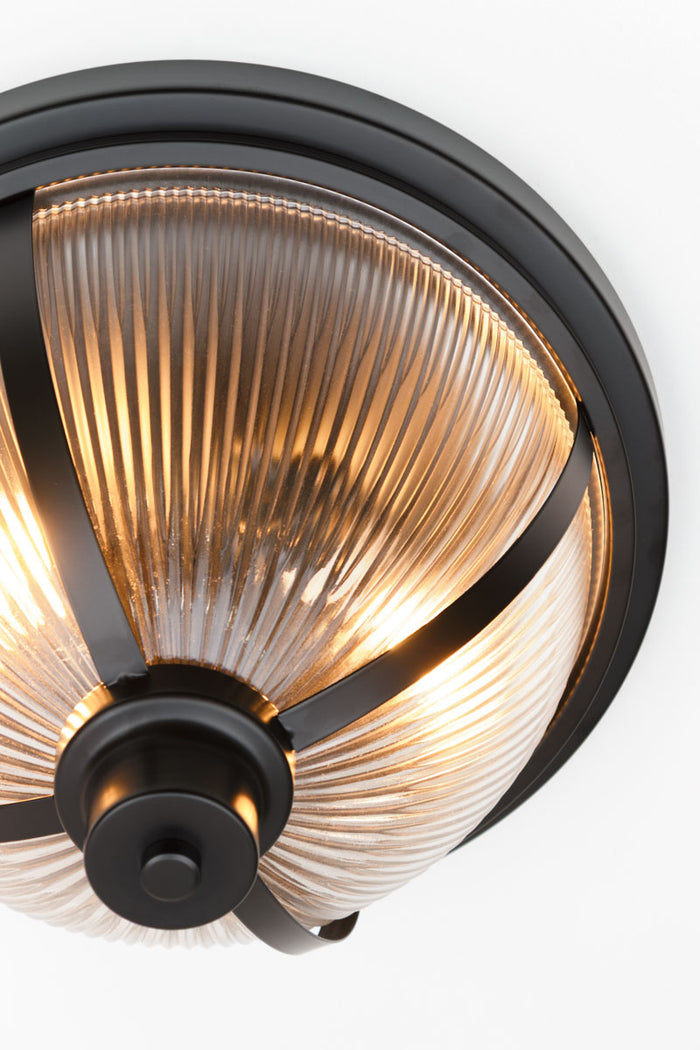 Close up of a ceiling light made up of a Reeded glass dome shade with black banded metal ware.
