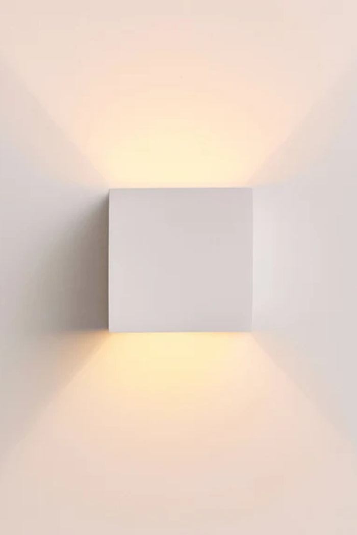 Front view of the illuminated Griffs Plaster Wall Sconce casting soft up and down light from its compact square plaster design.