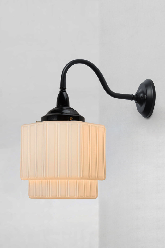 Art Deco inspirec glass shade in opal with vertical detailing, paired with a black gooseneck wall arm.