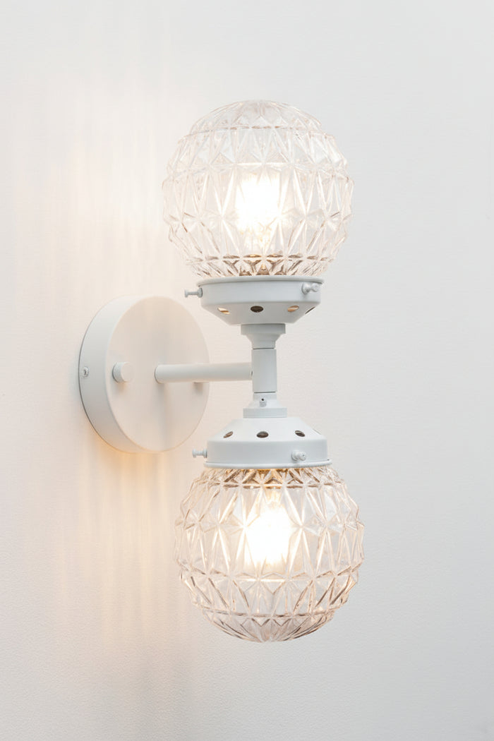 clear glass sphere with diamond cut points design on a white wall sconce with dual lampholders