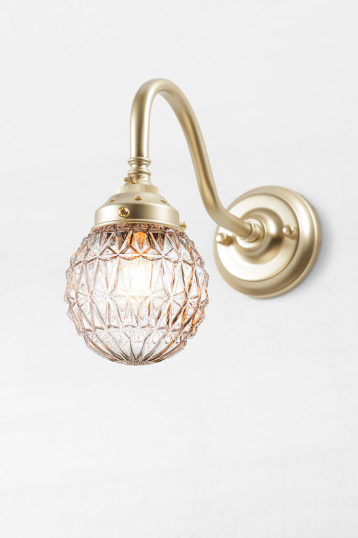 Glass ball shade with diamond cut detailing paired with a gold/brass gooseneck wall arm.