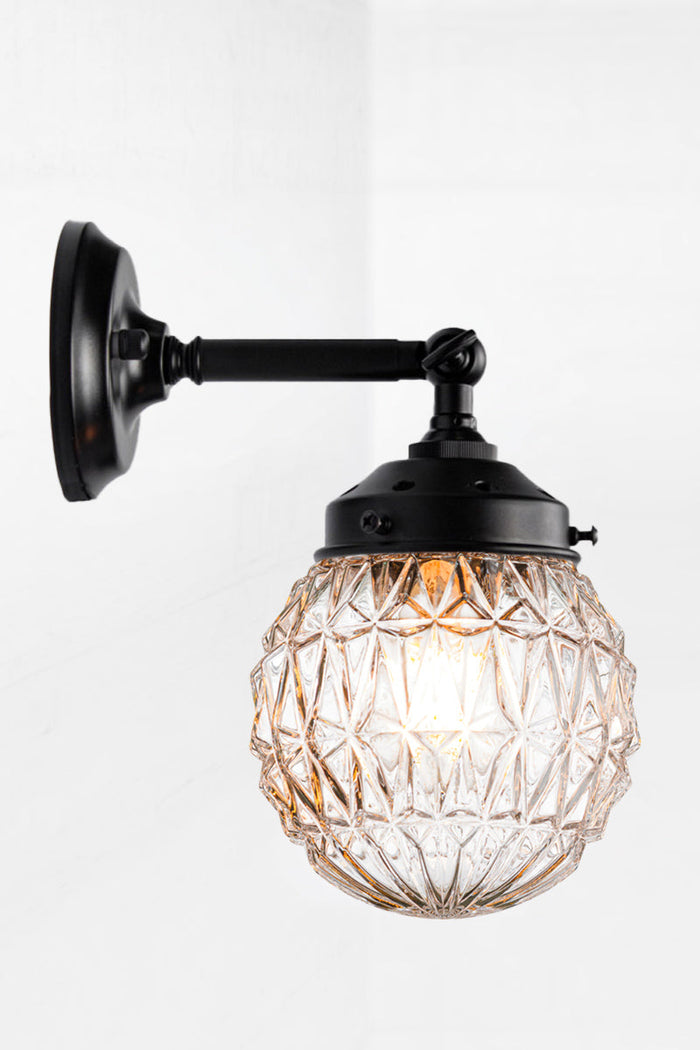 Short straight arm wall sconce with tiltable lampholder in black paired with a clear glass orb shade with vintage detailing.