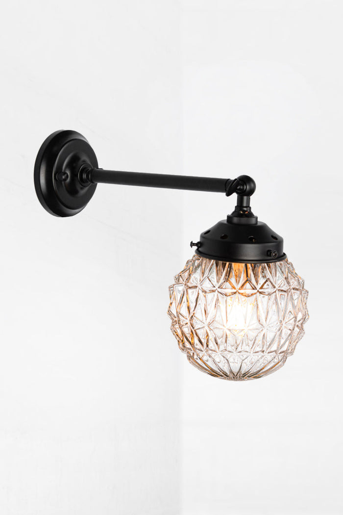 Long straight arm wall sconce with tiltable lampholder in black paired with a clear glass orb shade with vintage detailing.