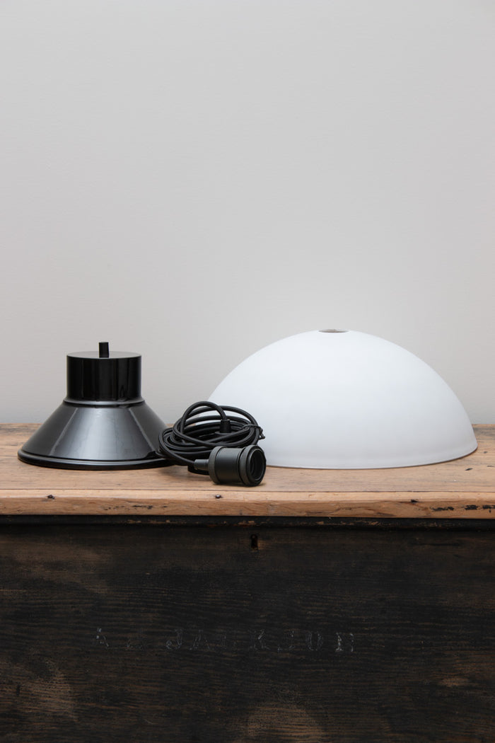 Uninstalled Homestead Foundry Pendant Light with a black shade cover and opal glass done shade, placed on a timber bench.