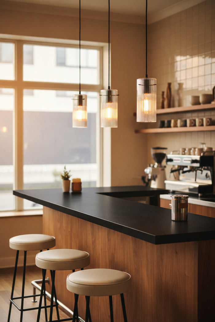 Three pendant lights featuring reeded clear glass and black pendant cords in a light filled kitchen with timber and black features.