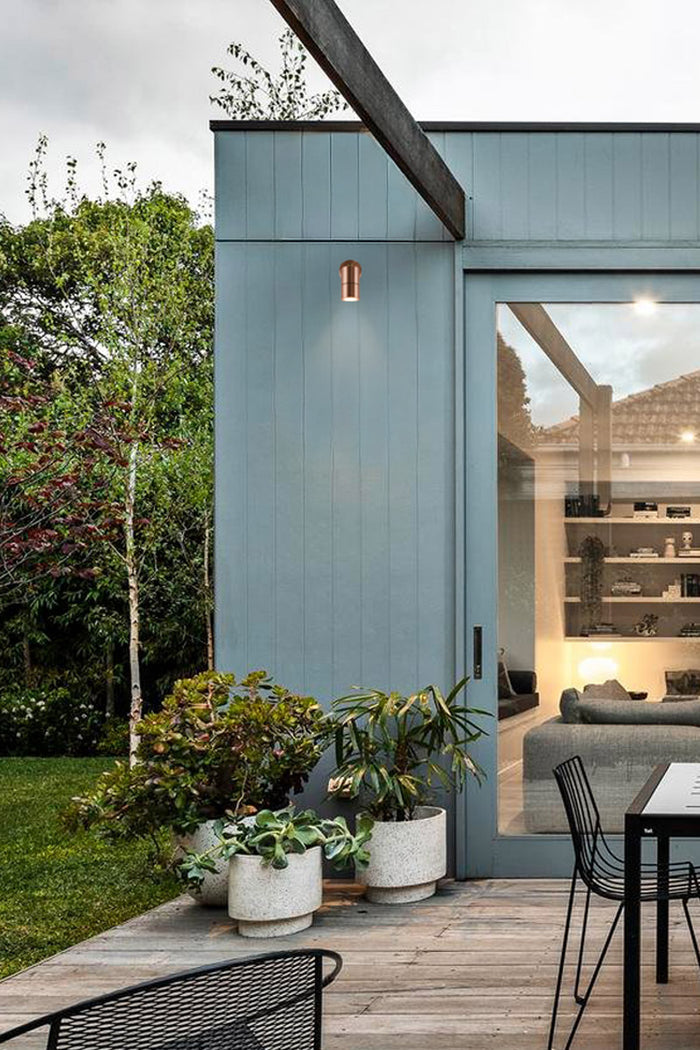 Polished copped adjustable spotlight on a blue outdoor wall of a modern garden space.