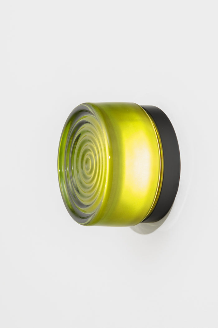 Green LED glass wall light illuminated against a white wall with vibrant green tinted glass and warm light output.