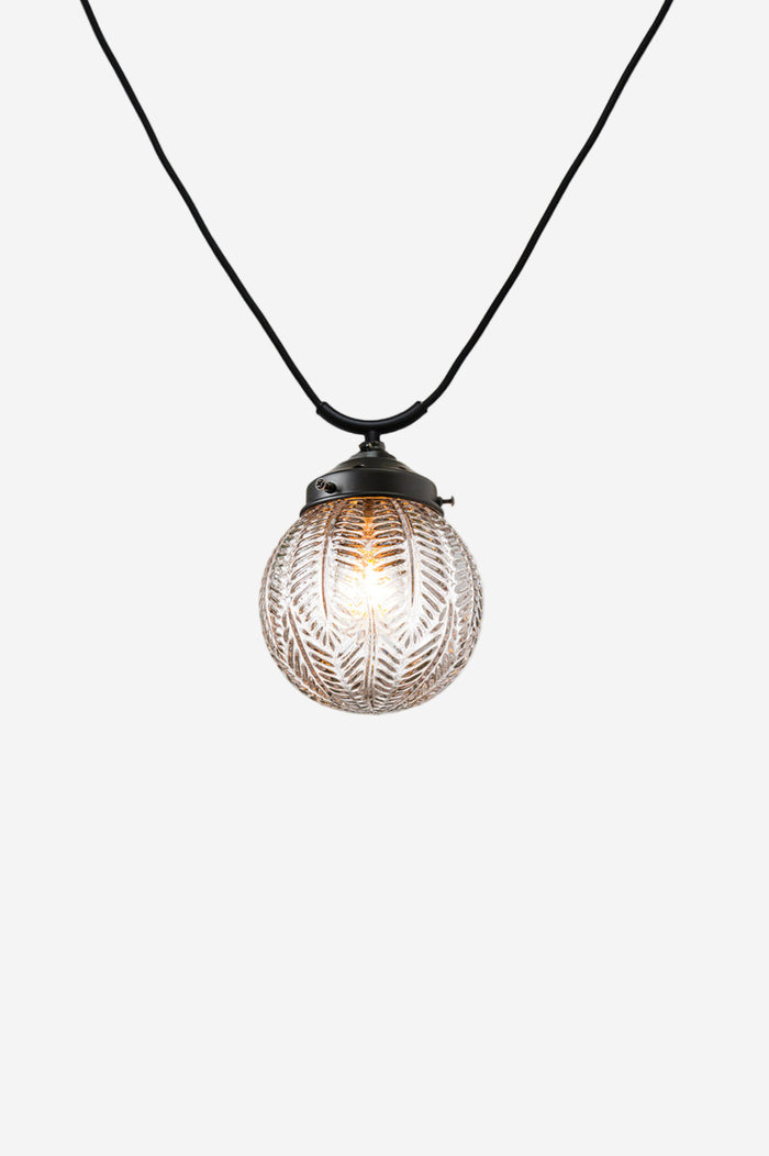 Glass shade with vintage detailing on a black trapeze pendant cord.