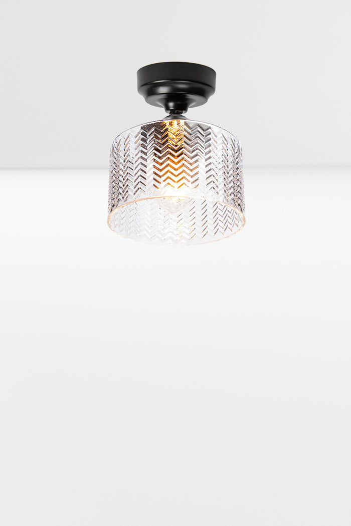 Cylindrical clear glass shade with a flat top and chevron detailing, paired with a black batten holder and gallery.