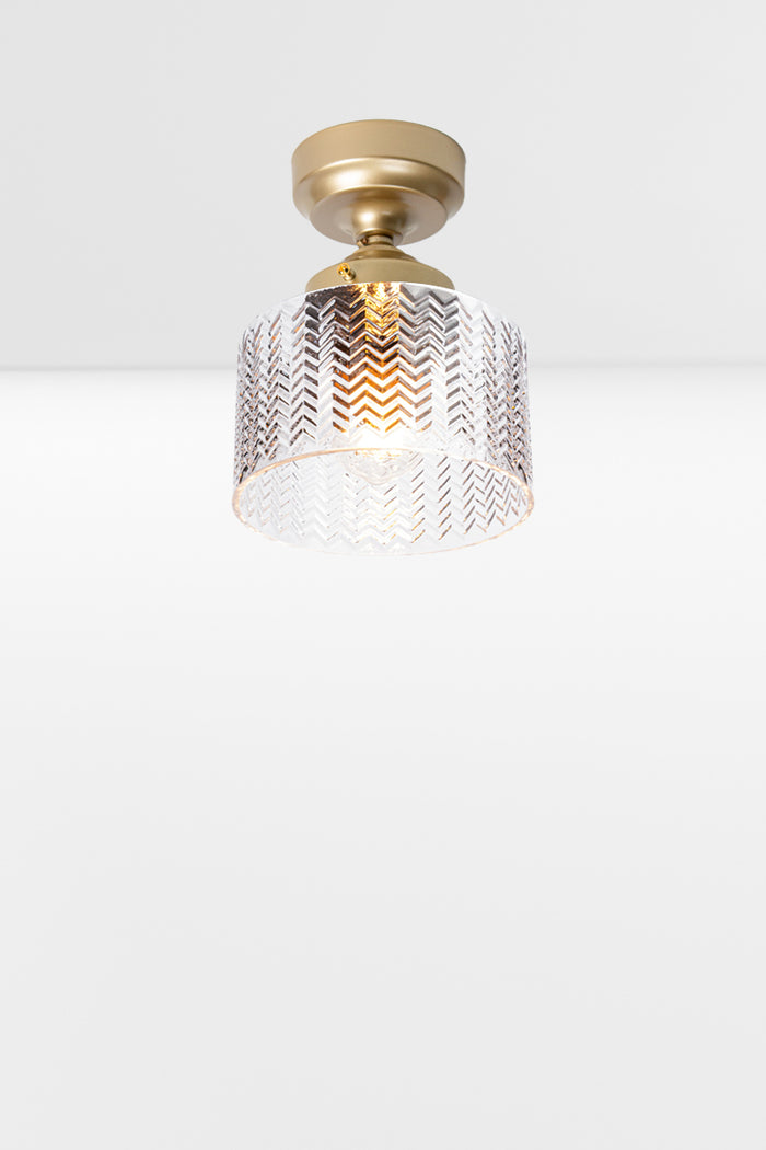 Cylindrical clear glass shade with a flat top and chevron detailing, paired with a gold/brass batten holder and gallery.