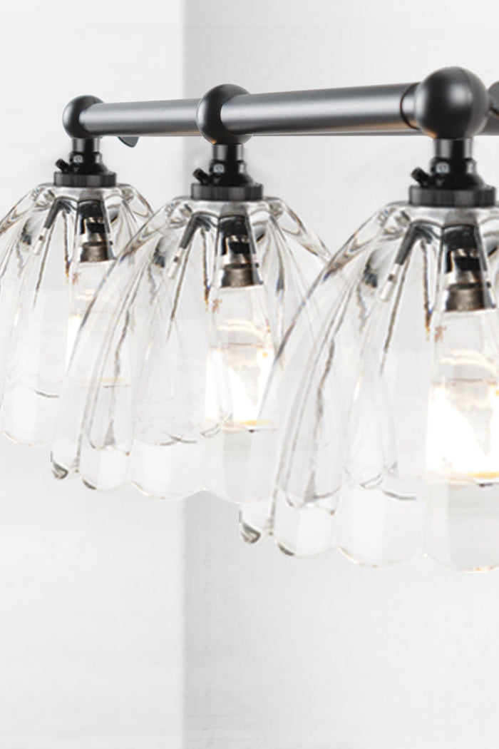 Black triple lamp wall sconce with clear, scalloped edge shades.