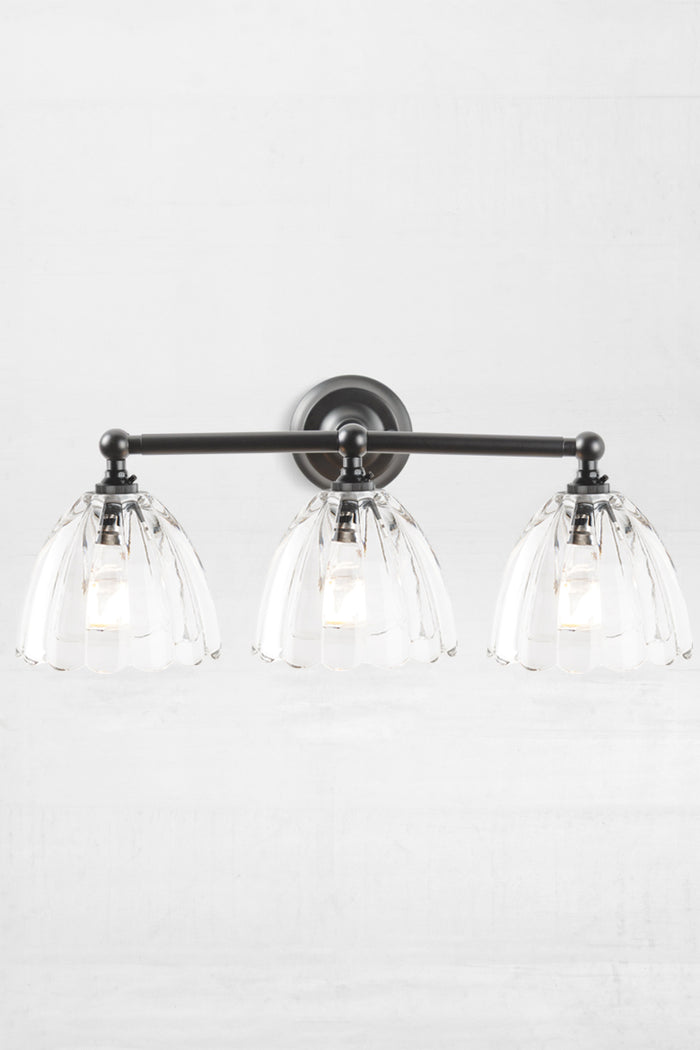 Black triple lamp wall sconce with clear, scalloped edge shades.