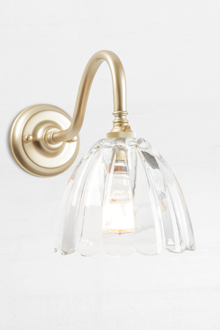 Gold/brass gooseneck wall sconce with a clear glass shade with a scalloped edge.