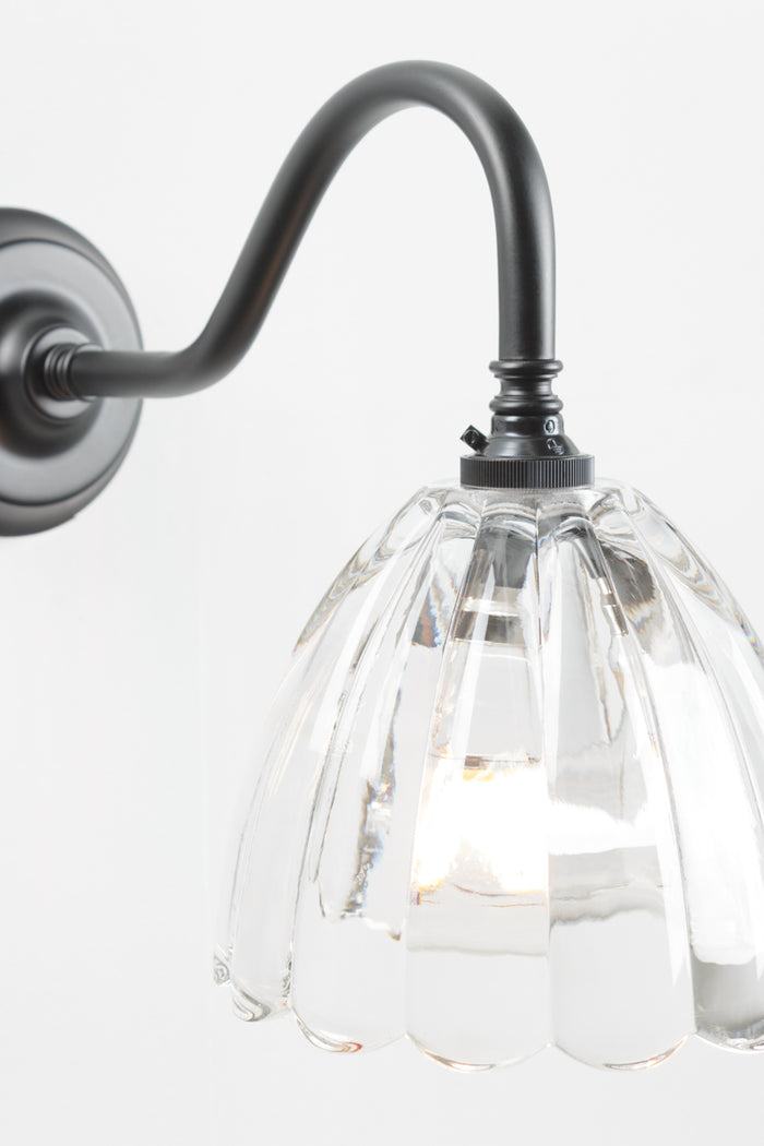 Close up of the black gooseneck wall sconce with a clear glass shade with a scalloped edge.