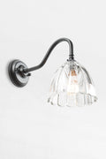 Black gooseneck wall sconce with a clear glass shade with a scalloped edge.