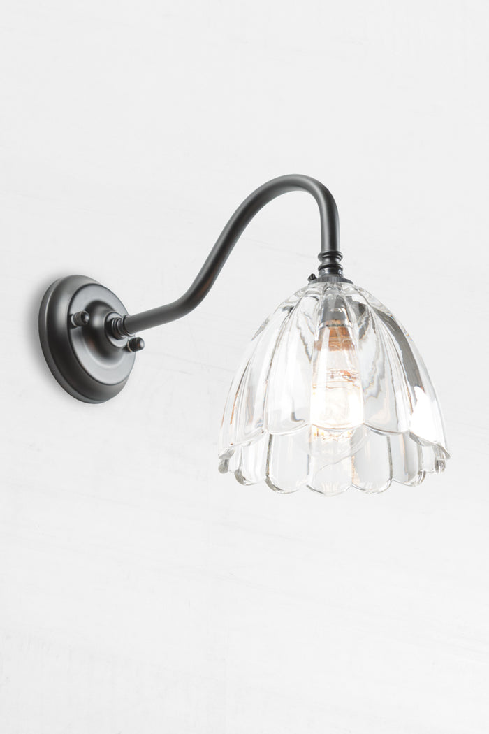 Black gooseneck wall sconce with a clear glass shade with a scalloped edge.