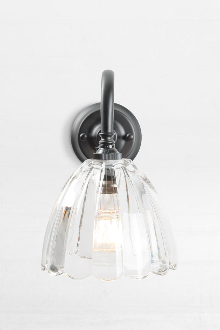 Front view of the black gooseneck wall sconce with a clear glass shade with a scalloped edge.