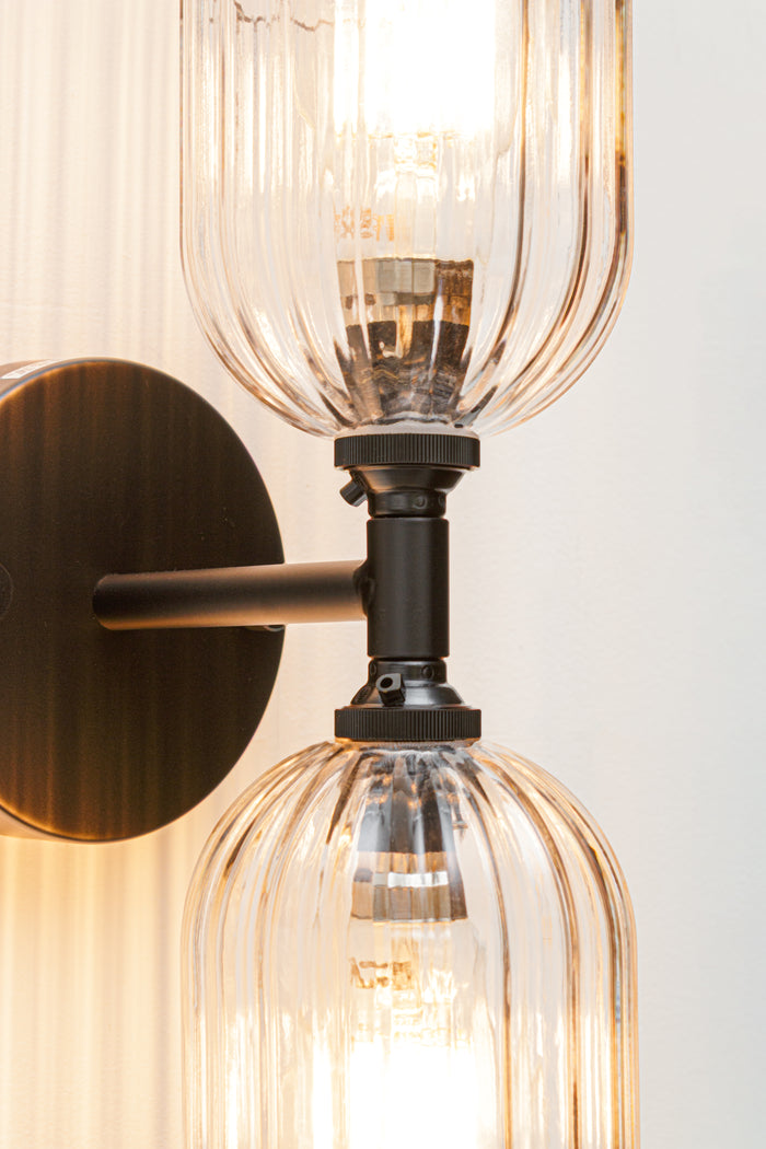 Close up of the black double wall sconce lampholders and two clear glass shades with fluted detailing.