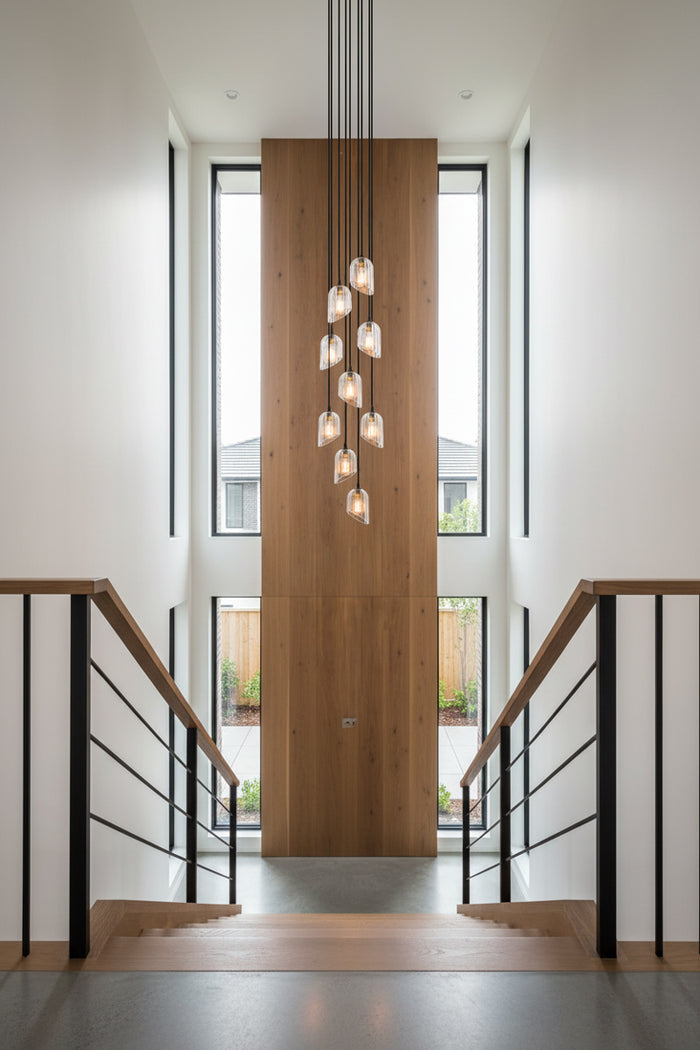 Entryway aith staircase, a 9 drop clear glass fluted shade chandelier with black cords.