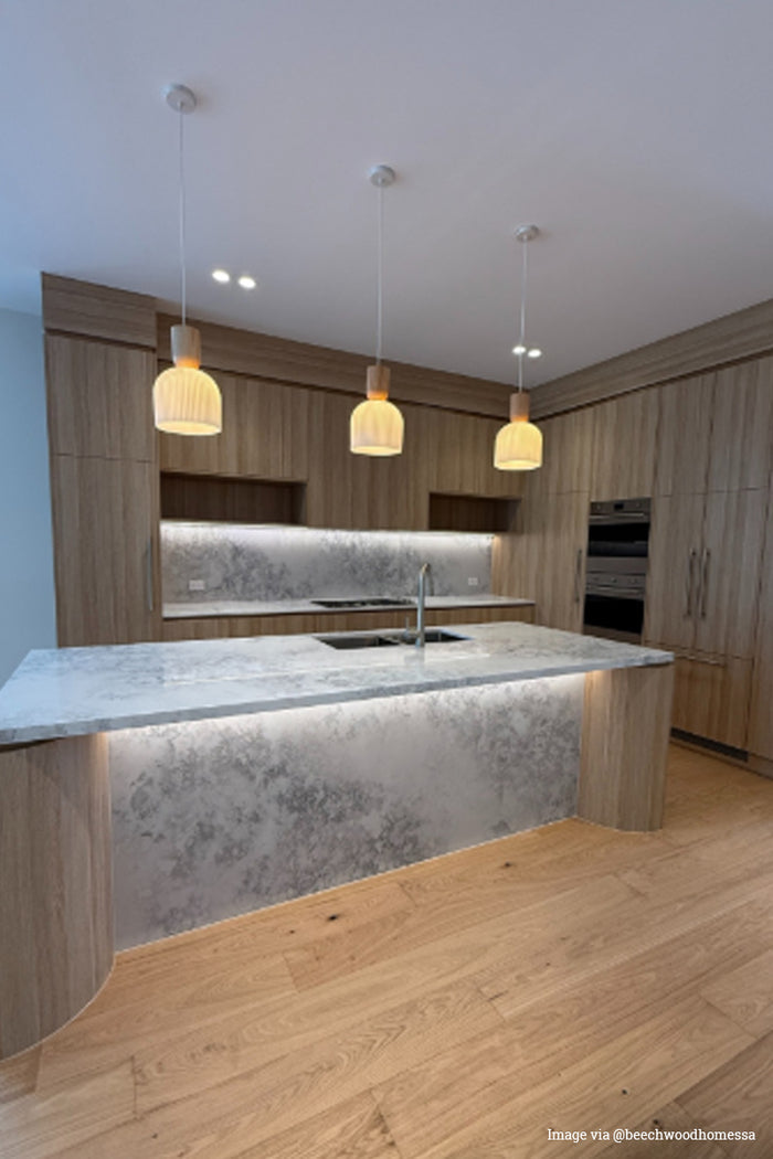 Image via @beechwoodhomessa: three wood detailed pendant cords that are paired with ceramic shades in a marble and wood kitchen.