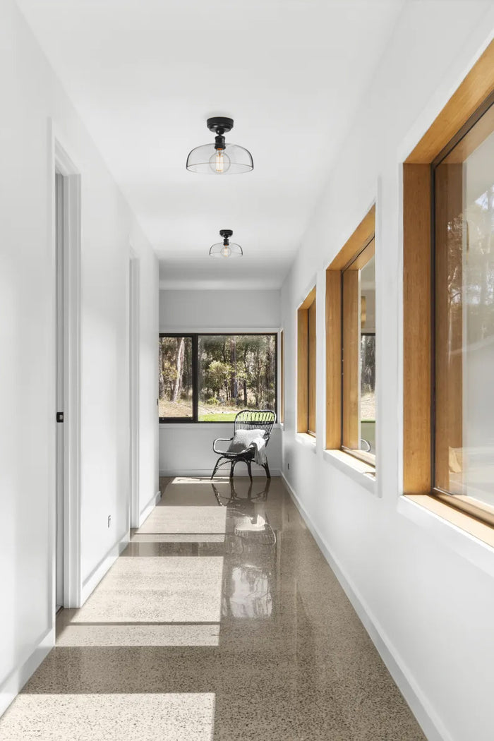 Beautiful window lined hallway with concreate floors white walls and timber accents- finished with two clear glass shades on black batten holders.
