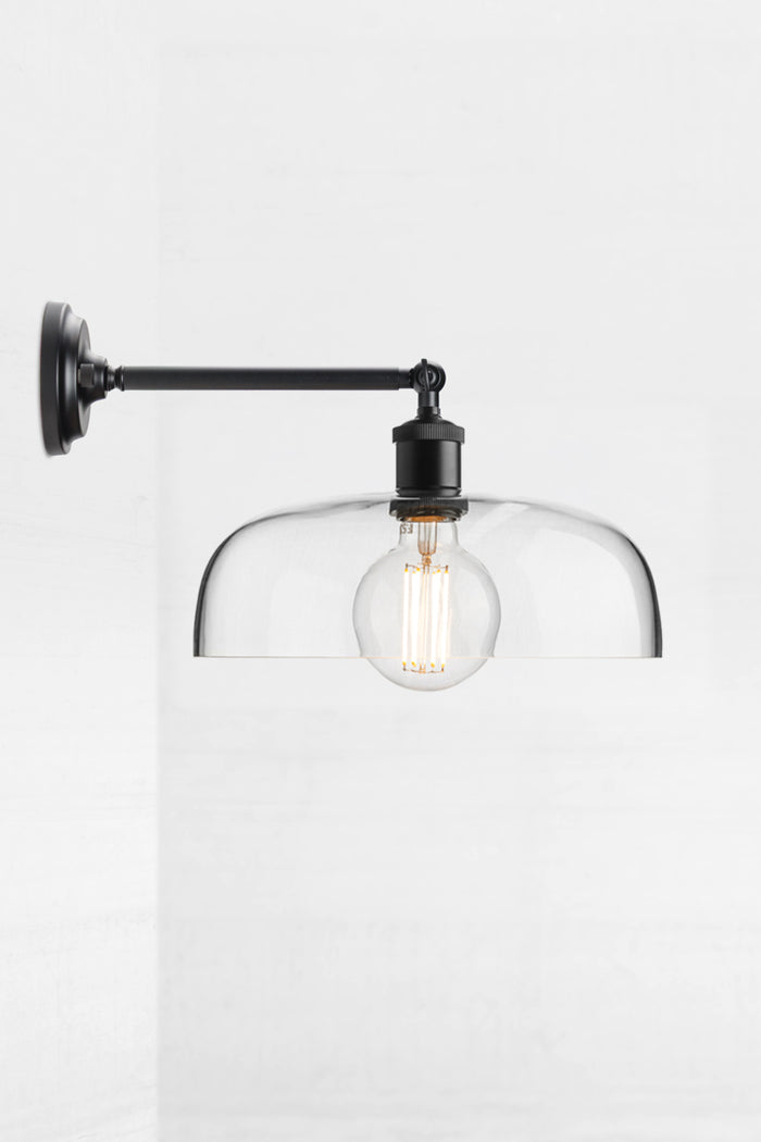 Black straight long arm wall sconce with swivel lampholder paired with a large clear glass shade and round bulb.