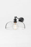 Black straight long arm wall sconce with a large clear glass shade and round bulb.
