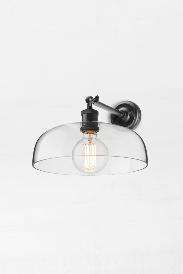 Black straight long arm wall sconce with a large clear glass shade and round bulb.