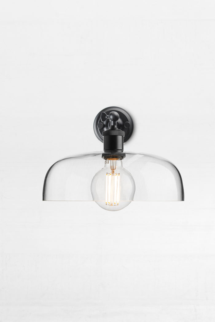 Front vire of the black straight wall sconce with swivel lampholder paired with a large clear glass shade and round bulb.