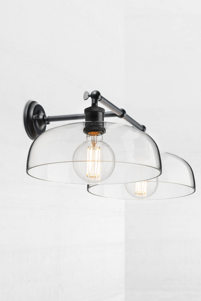 Black double swivel wall light, showing the knuckle joint, with two smooth clear glass shades.