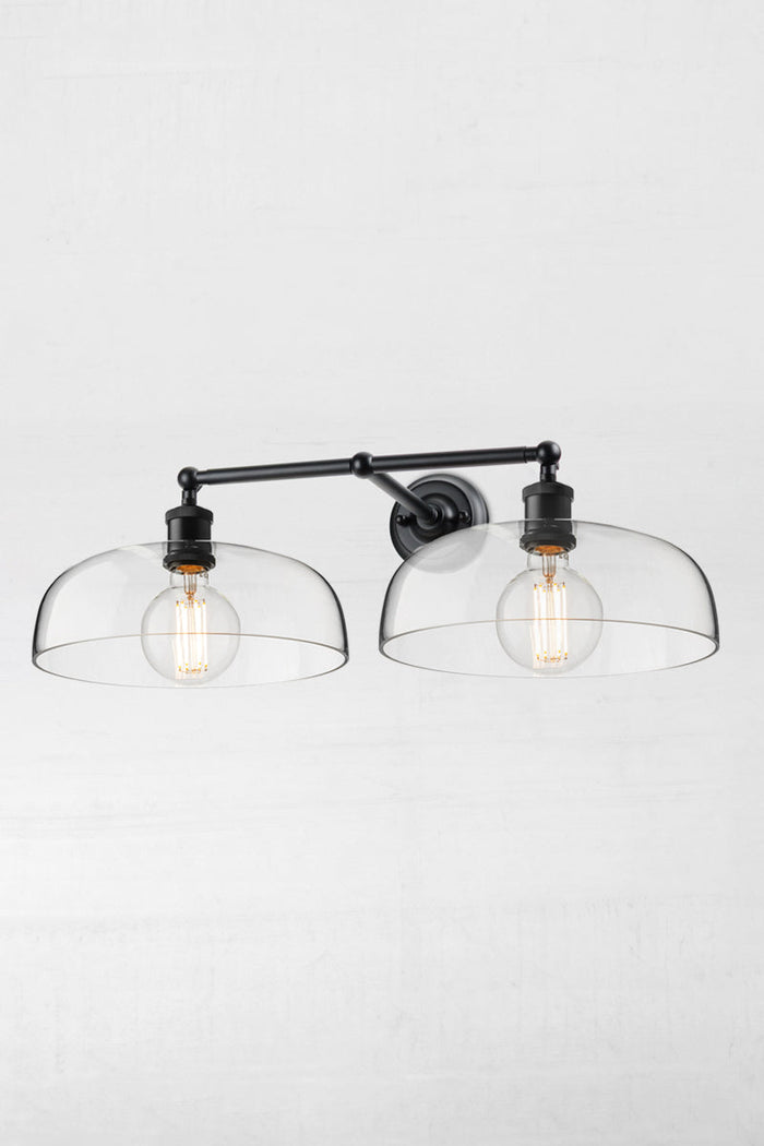 Black double swivel wall light with two smooth clear glass shades and round clear bulbs.