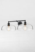 Black double swivel wall light with two smooth clear glass shades and round clear bulbs.