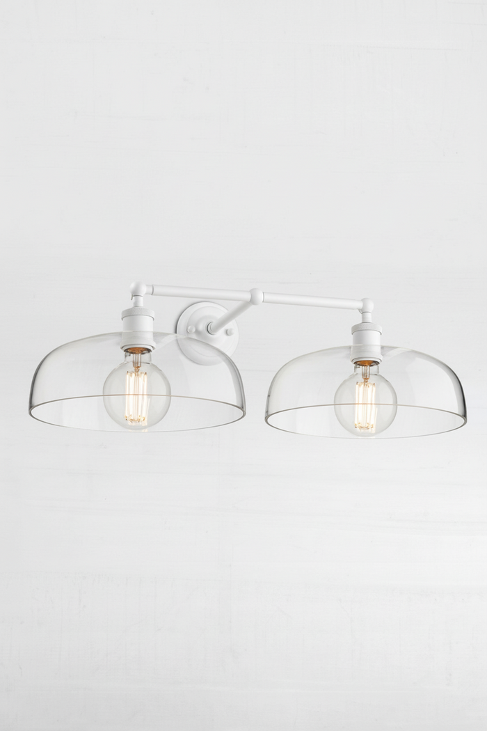 White double arm wall sconce with two clear glass shades.
