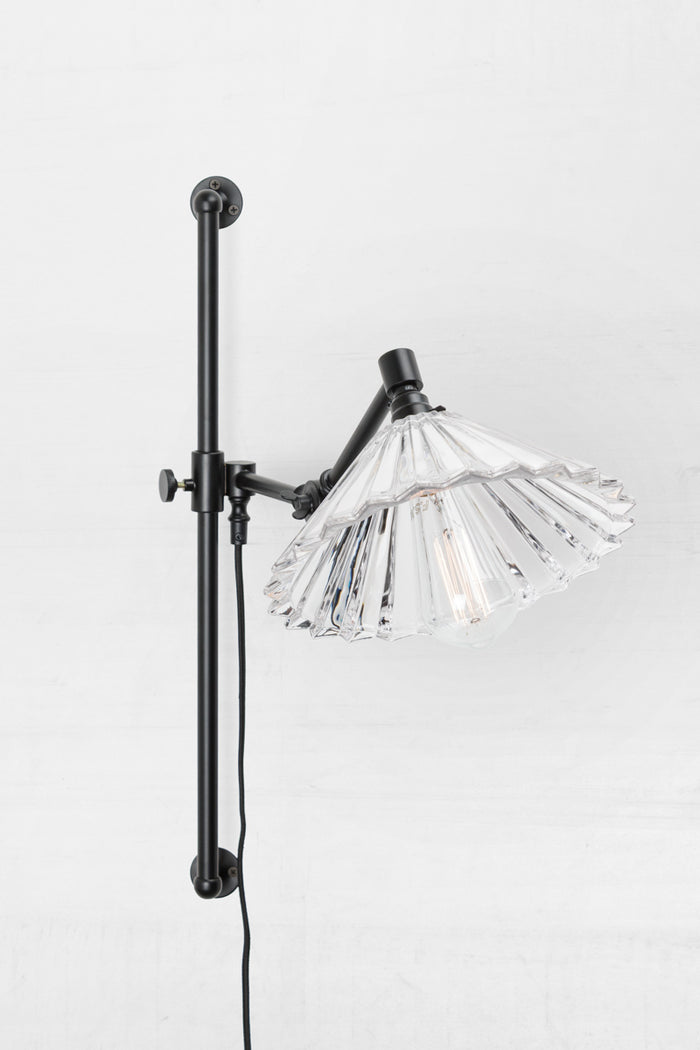 Clear glass pleated shade and black swing wall arm fixture, paired with a teardrop bulb.