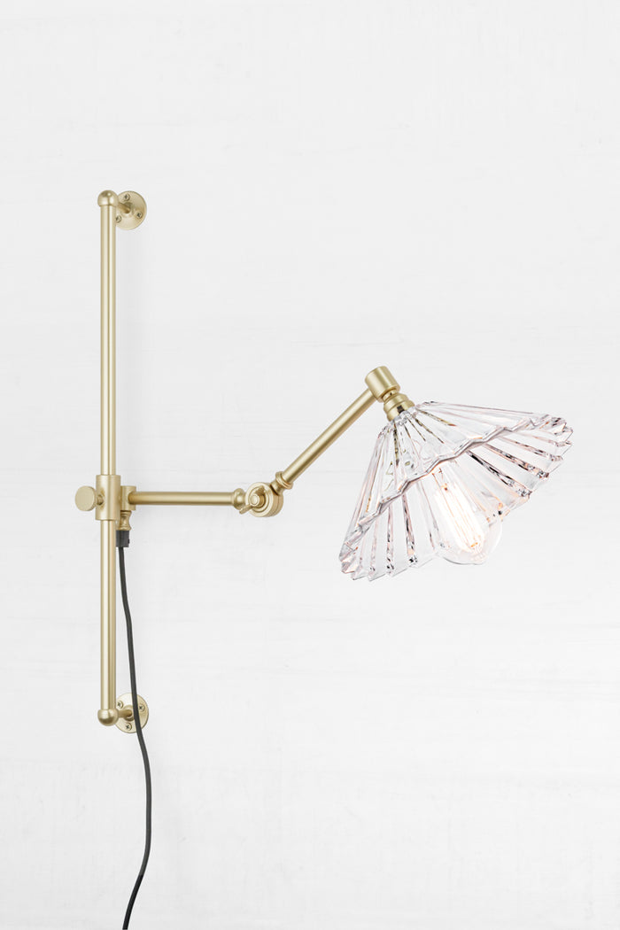 Gold/brass swing wall arm with wall plug and a clear glass pleated shade.