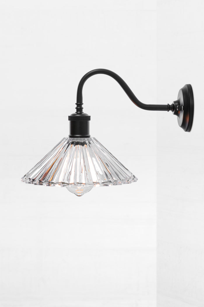 Side view of the pleated glass shade with a black gooseneck wall sconce and a clear teardrop bulb.