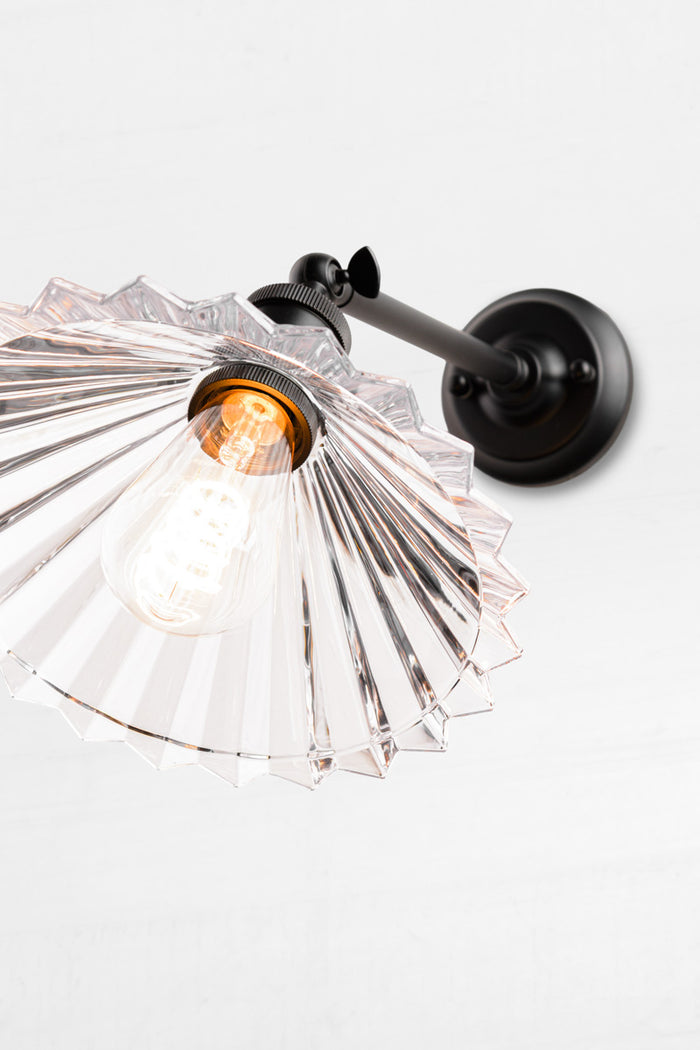Upward view of the clear glass pleated shade with clear teardrop bulb and black sconce.