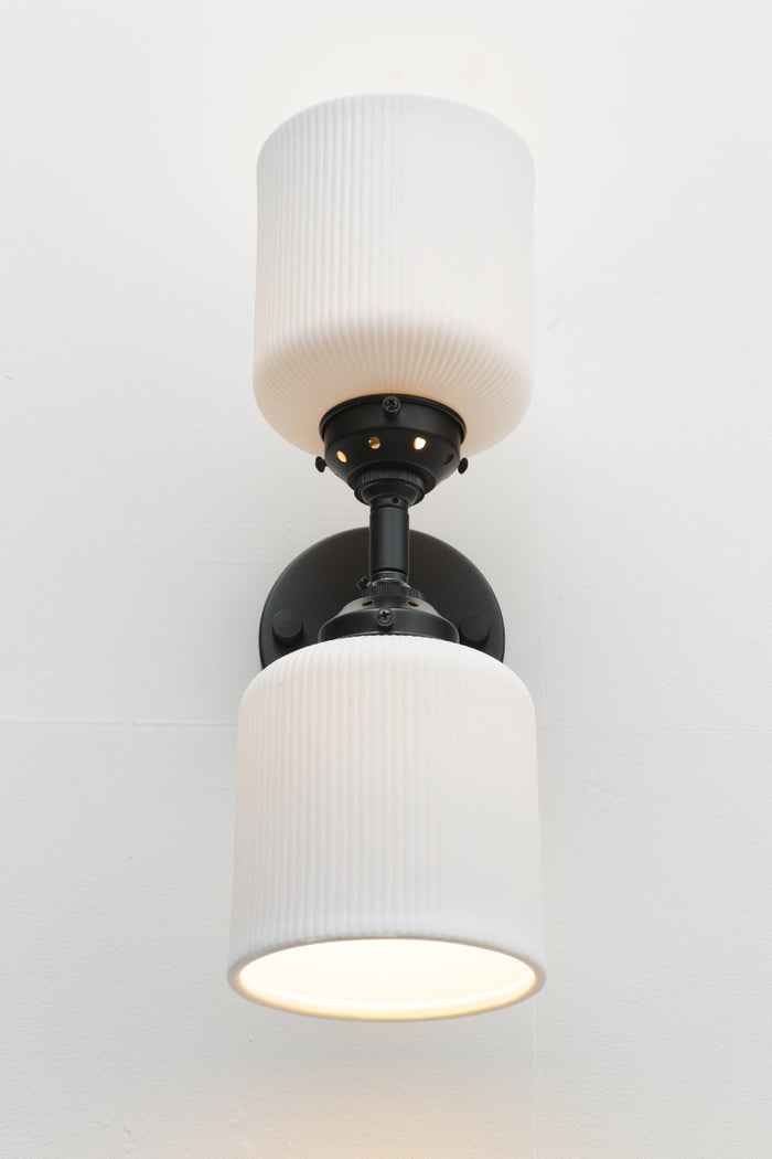 Front view of the black double wall sconce fixture paired with two unglazed white ceramic shades.