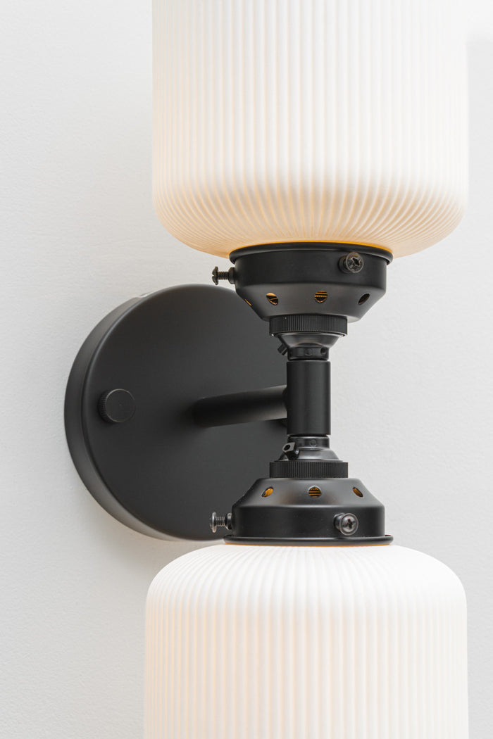 Close up of the black double wall sconce fixture paired with two unglazed white ceramic shades.