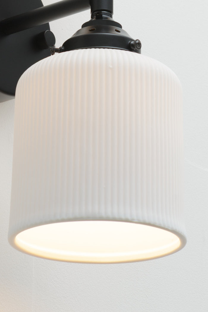 Wall sconce fixture with a black sconce paired with two unglazed white ceramic shades.