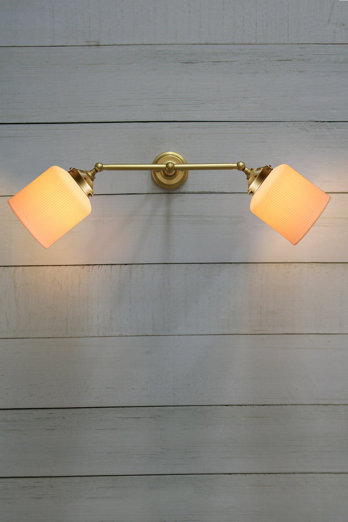 Double arm wall sconce in gold/brass with tiltable lampholders, paired with two white ceramic shades.