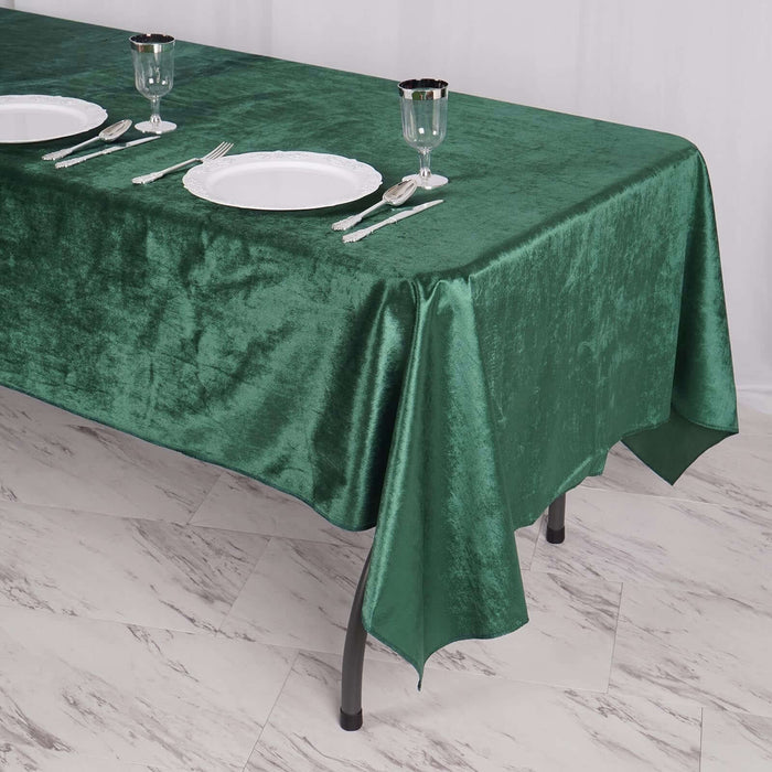 Green velvet tablecloth draped over a table with plates and glassware set.