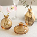 Set of three amber glass vases with flowers on a table.