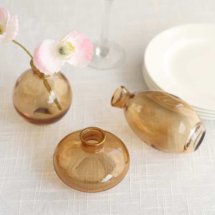 Three amber glass vases with flowers on a textured tablecloth.