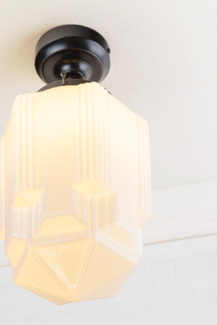 Close up of the large geometric opal glass shade with art deco influence, paired with a black batten holder.