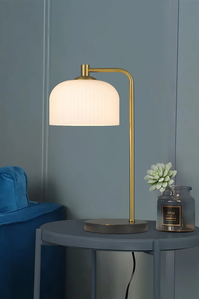 Table lamp with a ribbed opal glass shade, antique brass iron stande and solid marble base in black in a contemporary space.