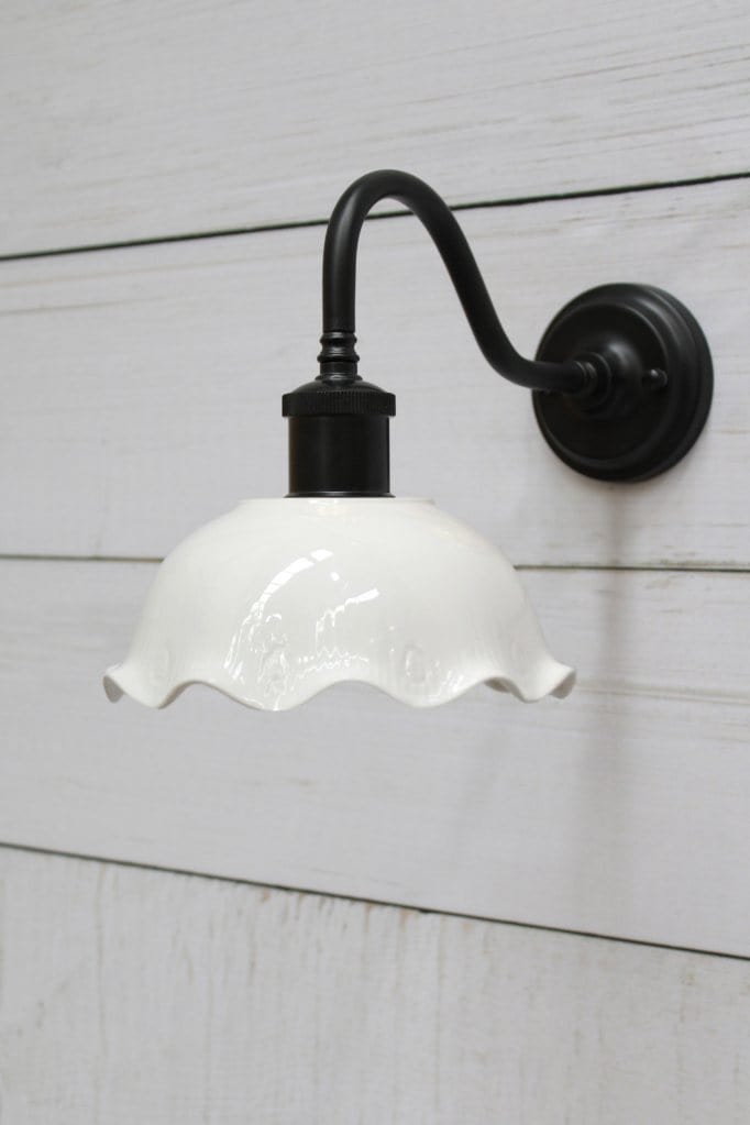 Ceramic gooseneck wall light with black arm affixed on wall.