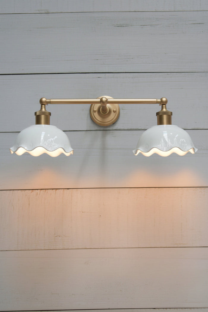 Gold/brass double swivel wall sconce with two white gloss ceramic shades with a frilled edge detail.